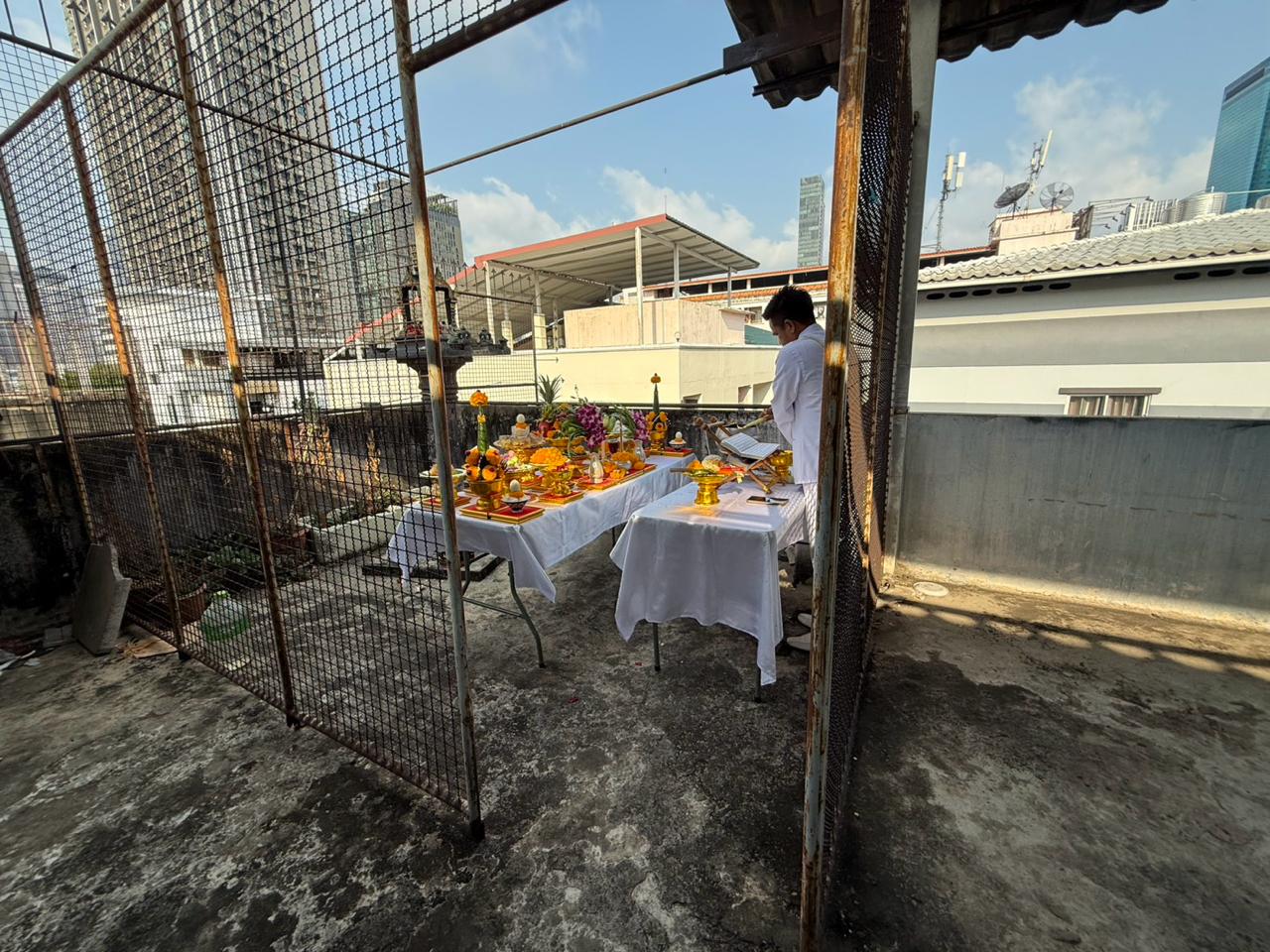 Ceremonial tables and offerings beside a mesh enclosure on the rooftop at WITHIN