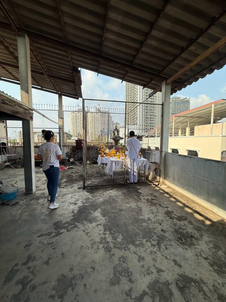 Two people approaching the rooftop ceremonial setup before removal of the spirit houses