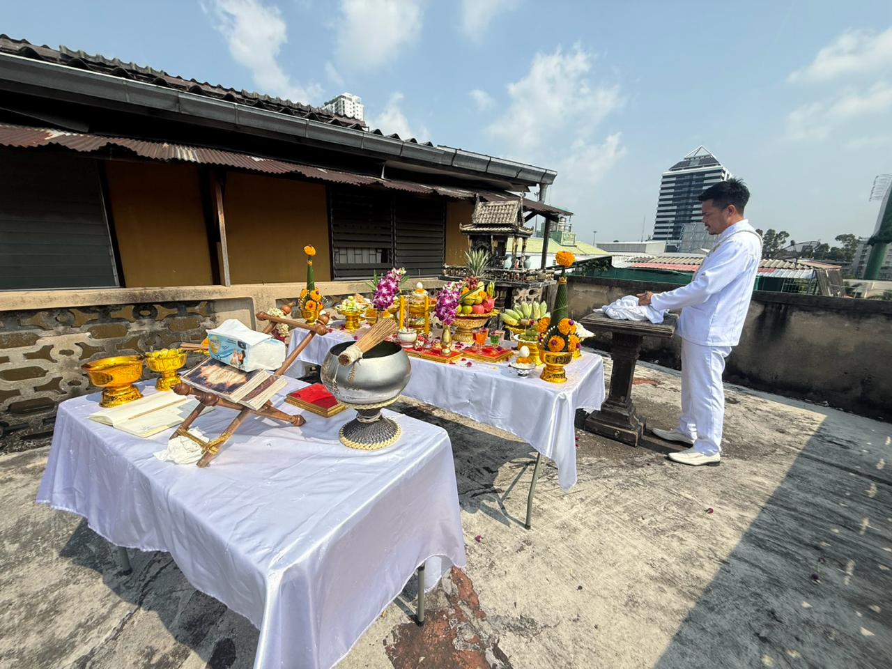 Rooftop ritual tables with offerings, books, incense, and a priest in white before the site works began