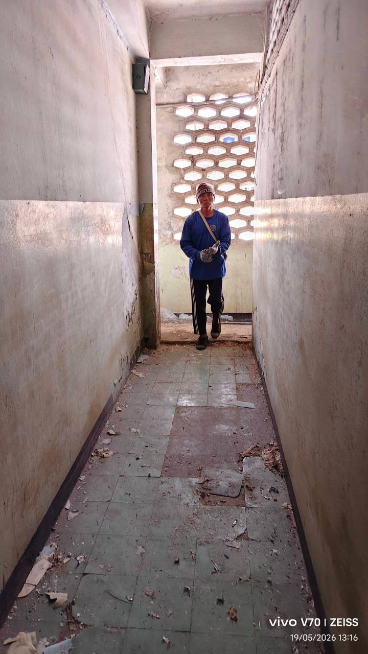 Dusty rear-building corridor with scattered debris and a worker during early pre-demolition clearing at WITHIN