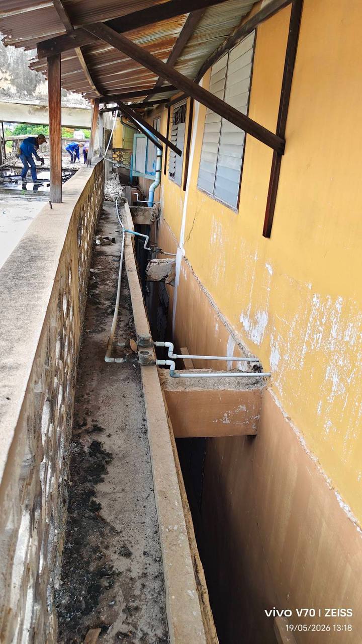 Side service corridor at the rear building showing exposed pipes, a narrow trench, and workers in the background during early clearance work