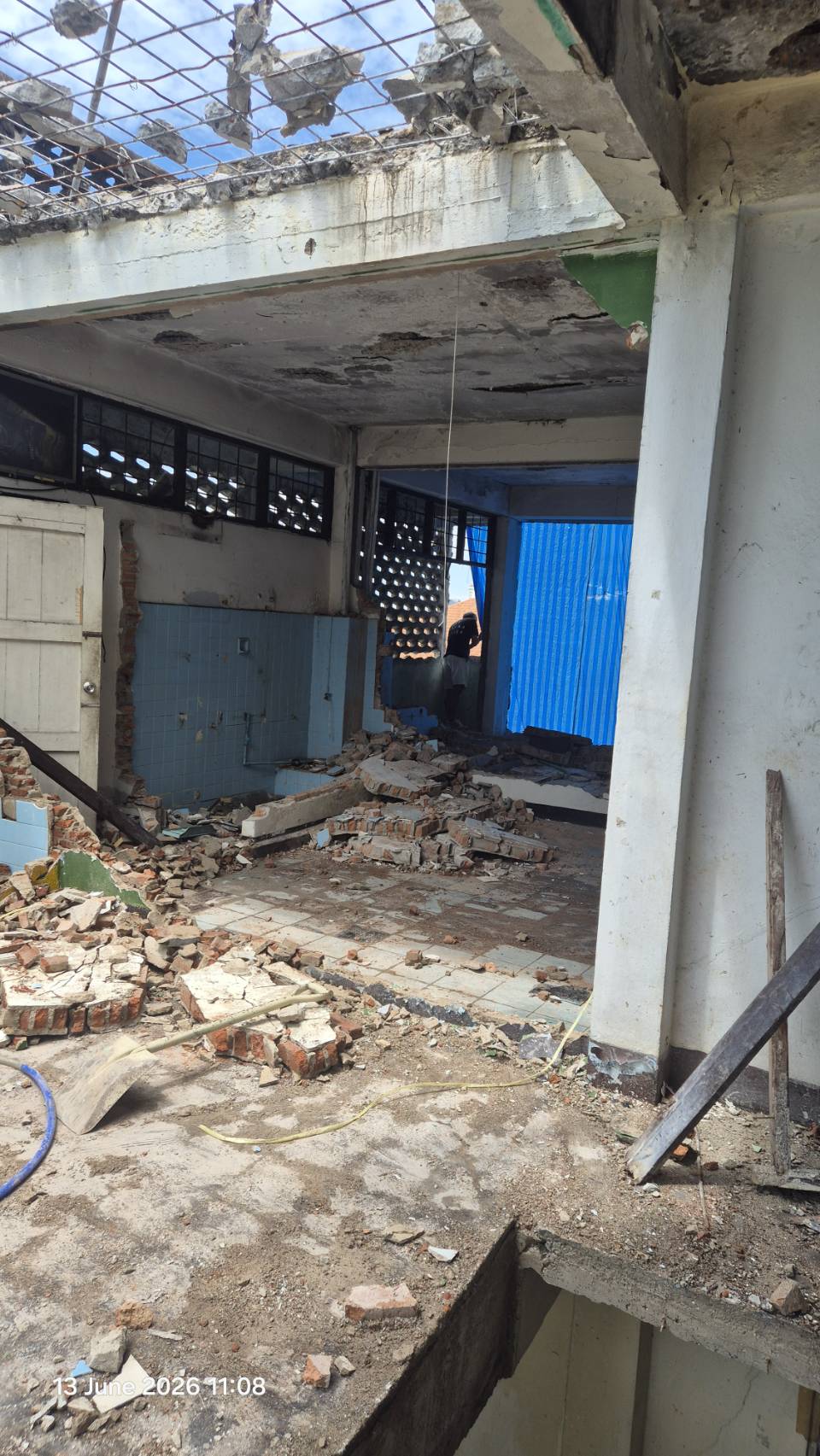 Second-floor room at WITHIN with partial roof opening above, broken wall sections, scattered debris, and structural columns still standing in place