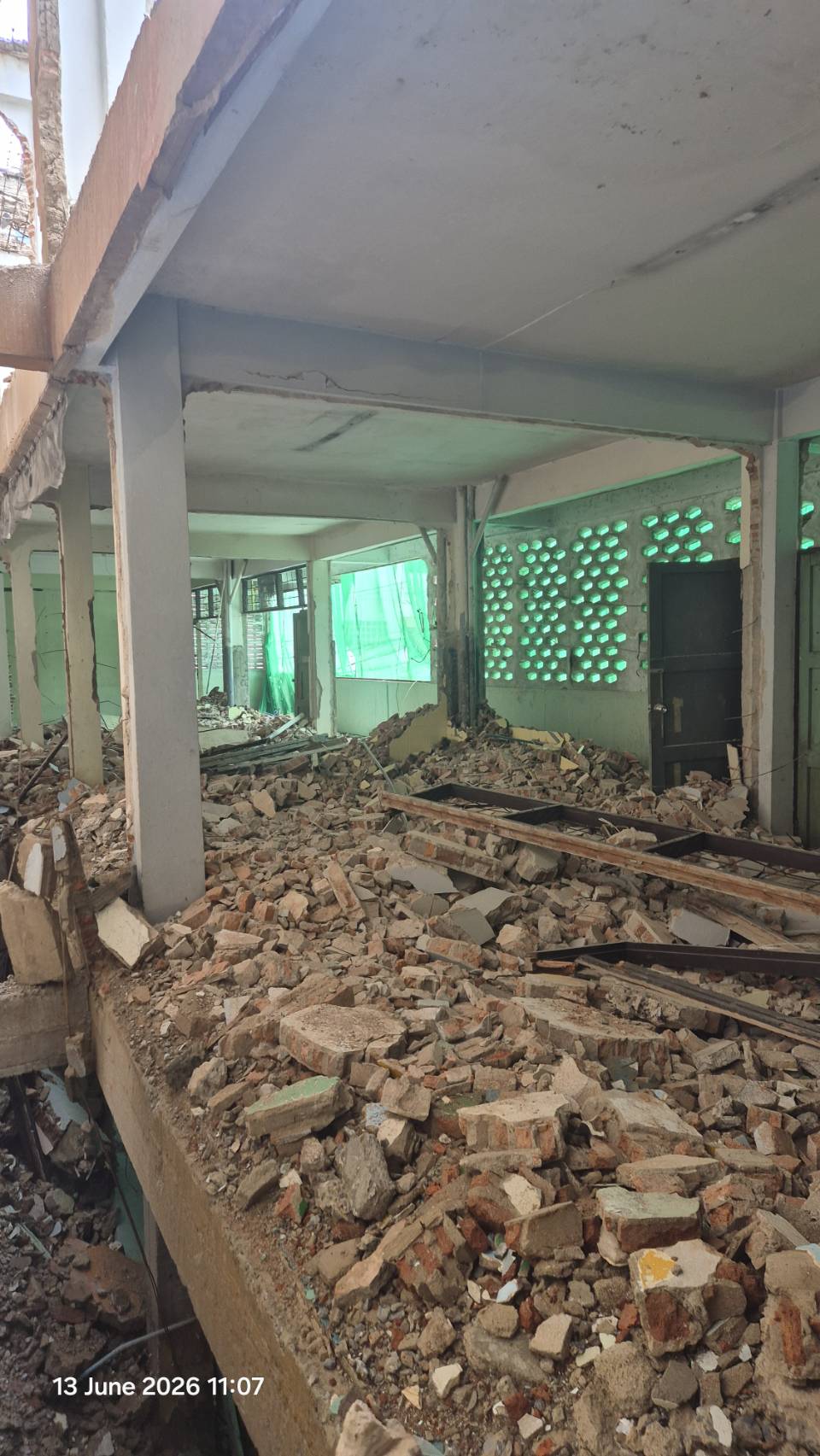 Second-floor corridor at WITHIN with a long rubble field, exposed slab edge, broken wall sections, and temporary green screening at the perimeter