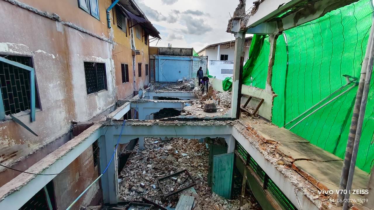 Long side view through the demolition zone at WITHIN showing open slab edges, heavy rubble below, and the building cut through along its length