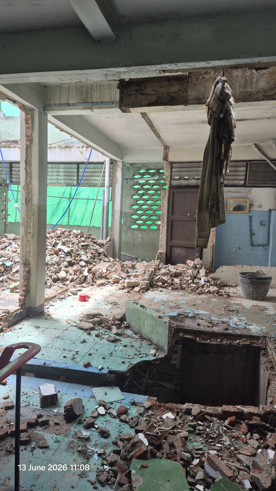 Interior demolition view at WITHIN with broken tiled floor, a large void cut through the slab, and rubble spread across the room
